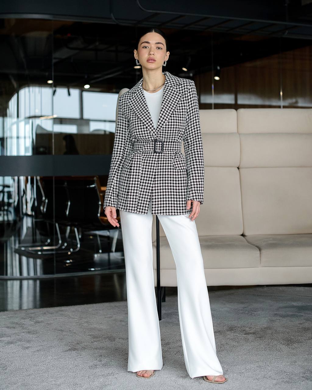Person wearing a black and white checkered blazer and white pants in an indoor setting.