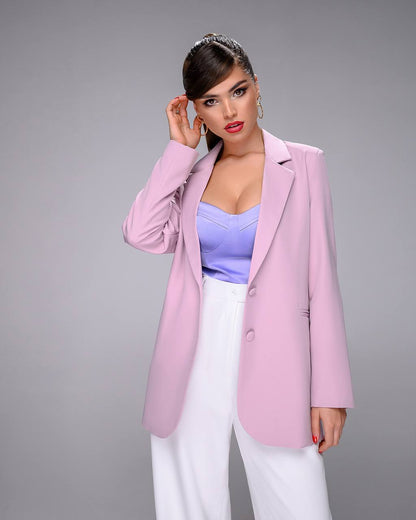 Woman wearing a pink blazer over a purple top and white pants on a gray background