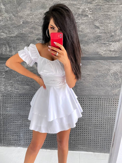 Woman in a white dress taking a mirror selfie against a gray wall.