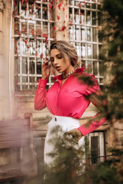 Woman wearing a bright pink blouse and white skirt outdoors with a blurred background