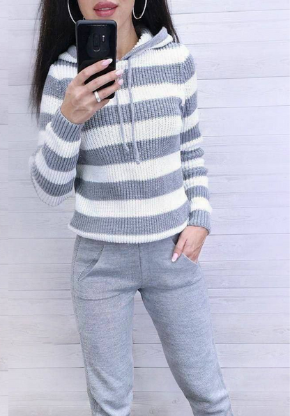 Person wearing a gray and white striped sweater and gray pants against a light wooden background.
