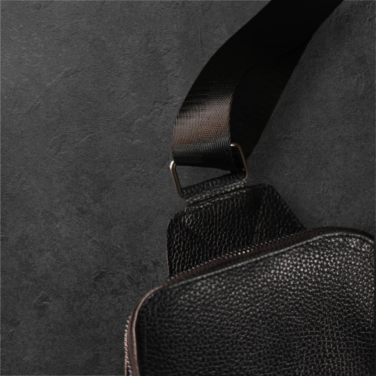 Close-up of a black pebbled leather bag with a matching black woven strap and metal hardware, set against a dark textured background.