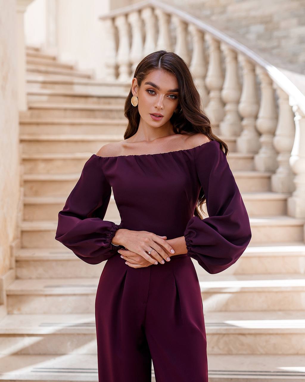 Woman wearing a purple off-shoulder outfit standing on a staircase.