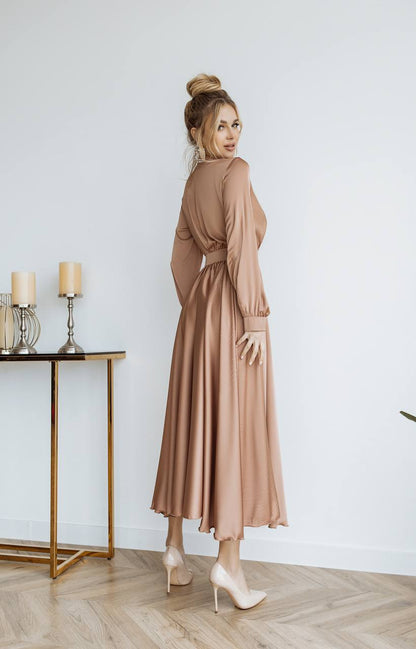 Woman in a beige dress standing in a room with a table and candles.
