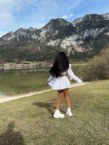 Person in a white outfit standing by a lake with mountains in the background