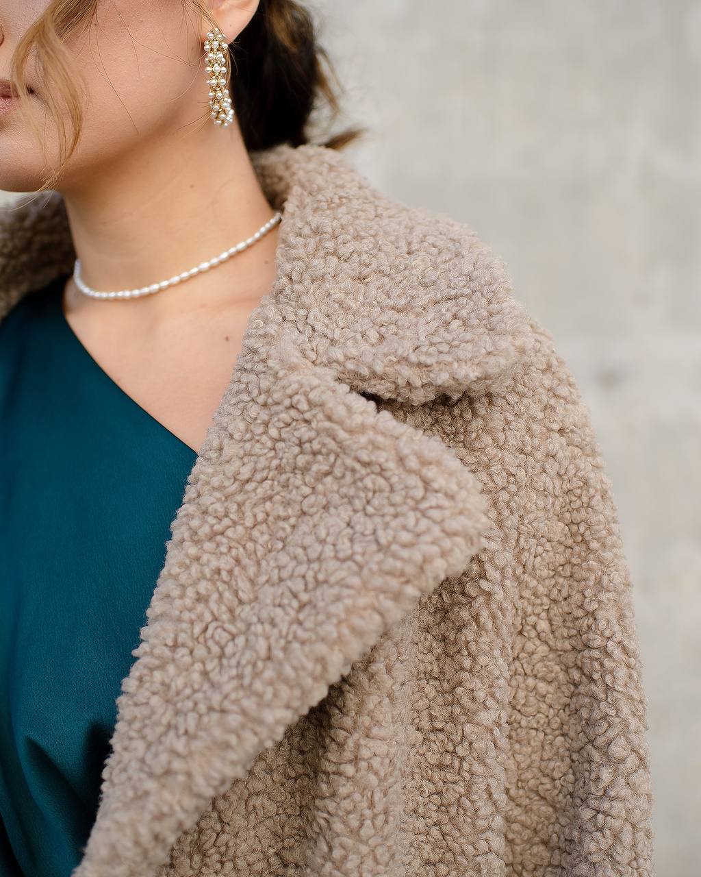 Close-up of a person wearing a beige sherpa coat with a blurred background
