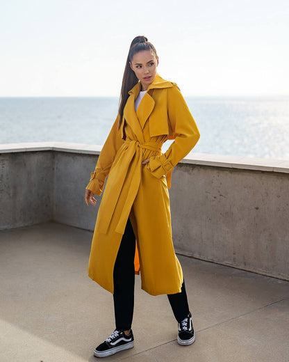Woman wearing a yellow trench coat standing on a rooftop with ocean view