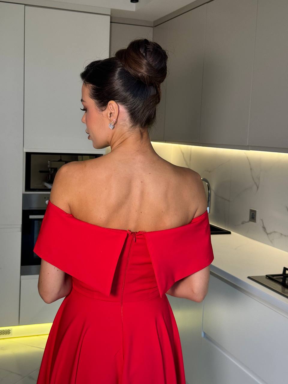 Woman in a red off-shoulder dress standing in a modern kitchen.