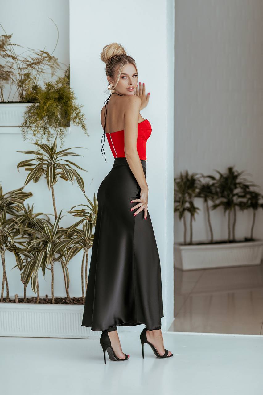 Woman in a red top and black skirt posing in a room with plants.