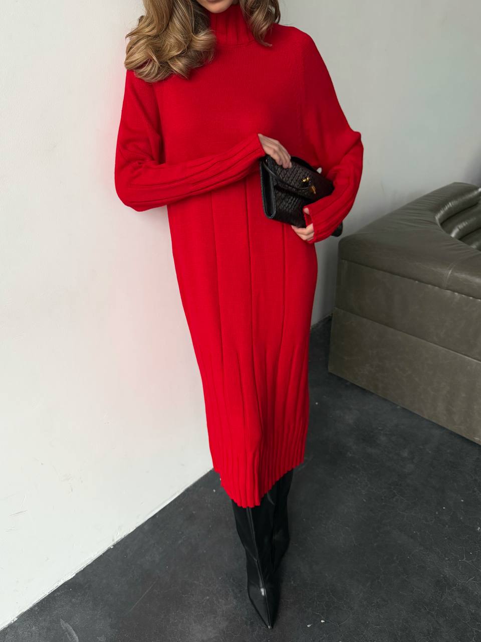 Person wearing a red dress with black boots against a white wall.