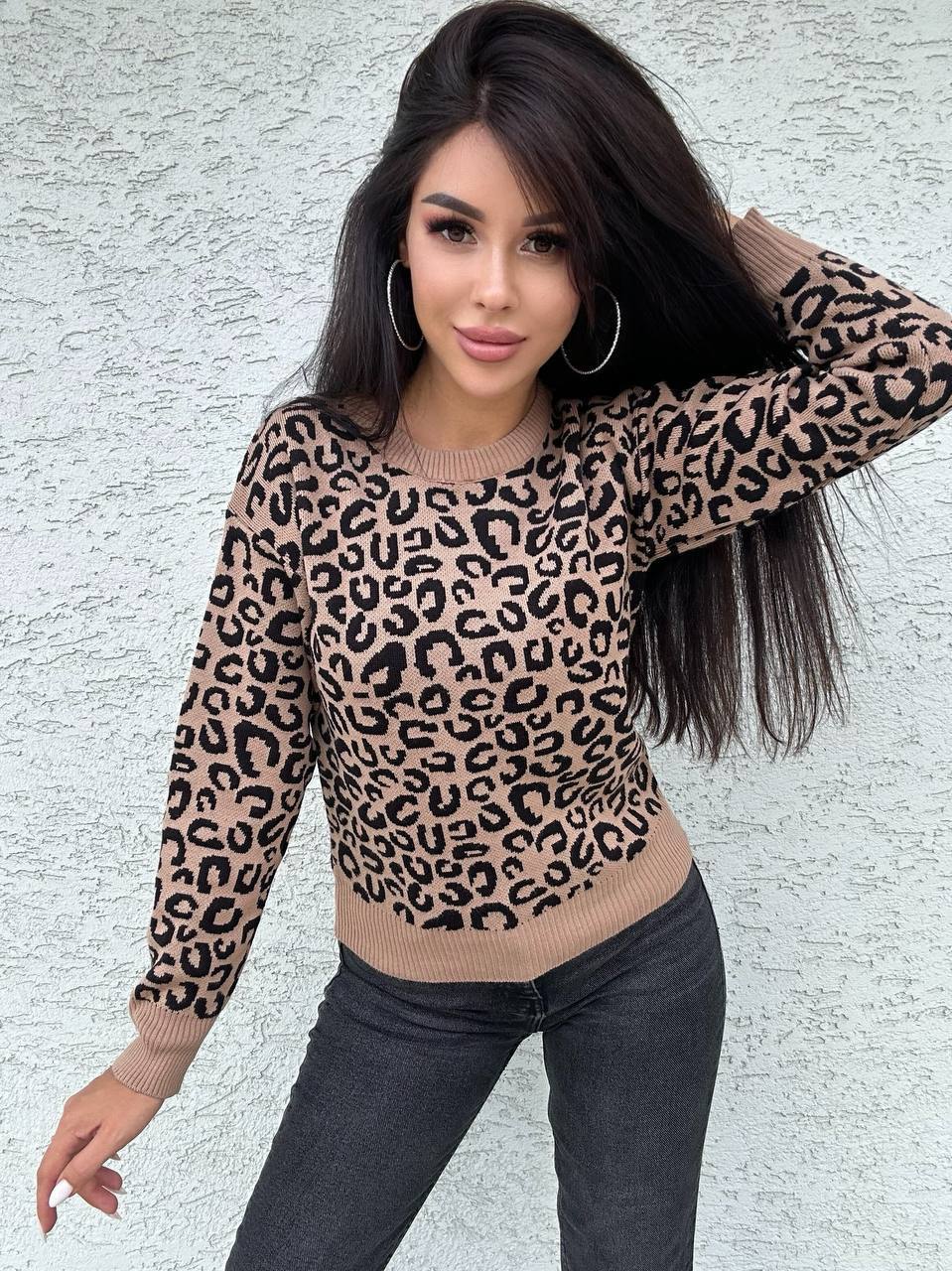Woman wearing a leopard print sweater against a textured wall.