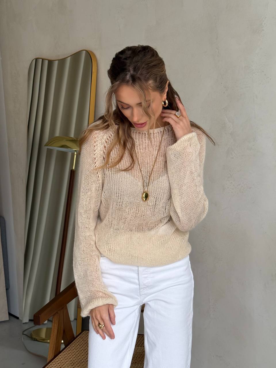 Woman wearing a beige sweater and white pants against a neutral background