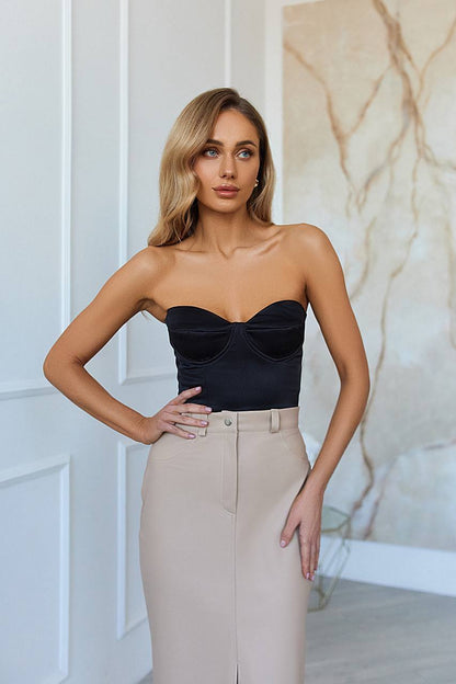 Woman wearing a black strapless top and beige pants against a marble wall.