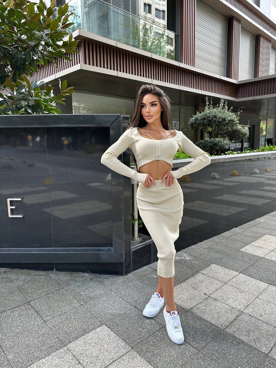 Woman in a white outfit standing on a sidewalk with modern buildings in the background