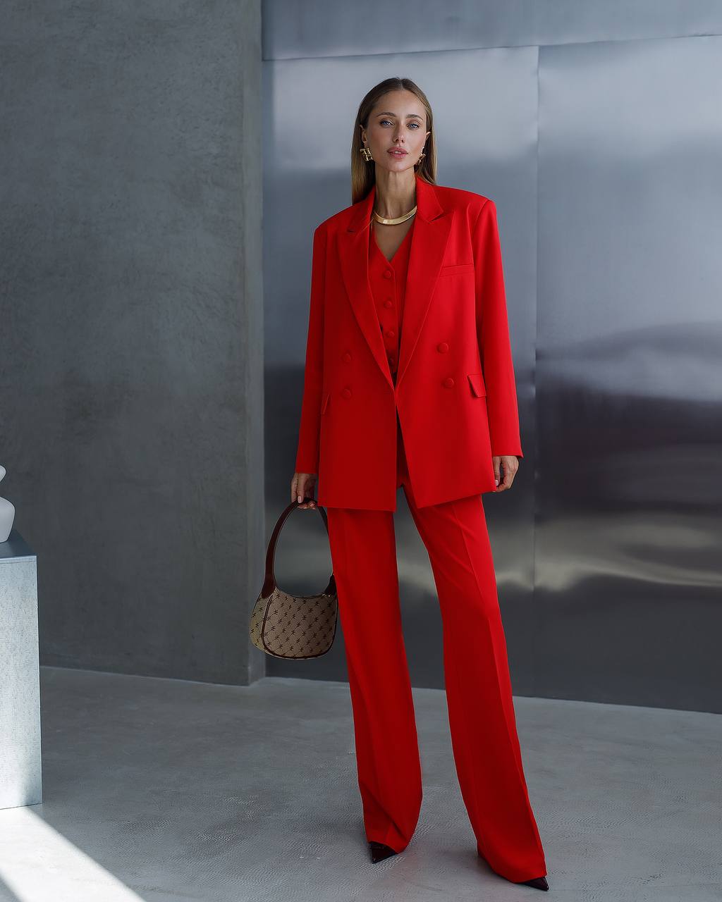 Woman in a red suit holding a patterned handbag against a gray background