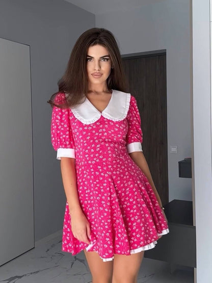 Woman wearing a pink floral dress with a white collar in an indoor setting