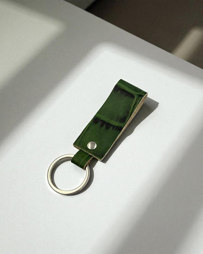 A green leather keychain with a silver metal key ring, resting on a white surface under direct sunlight.