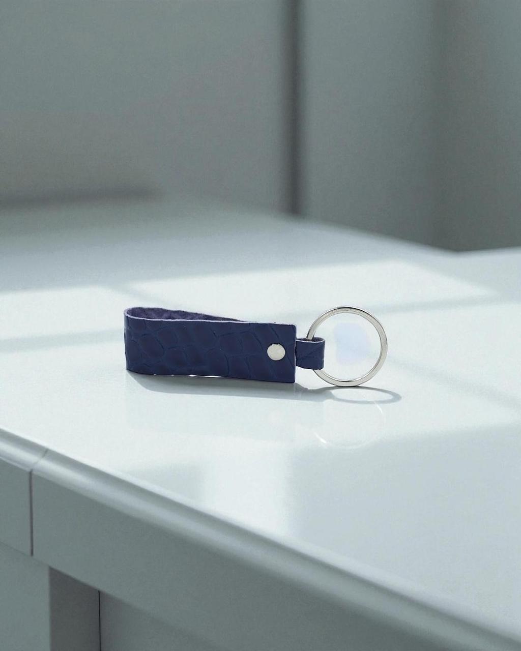 A dark blue textured leather keychain with a silver metal key ring, resting on a clean white surface.