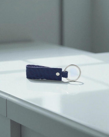 A dark blue textured leather keychain with a silver metal key ring, resting on a clean white surface.