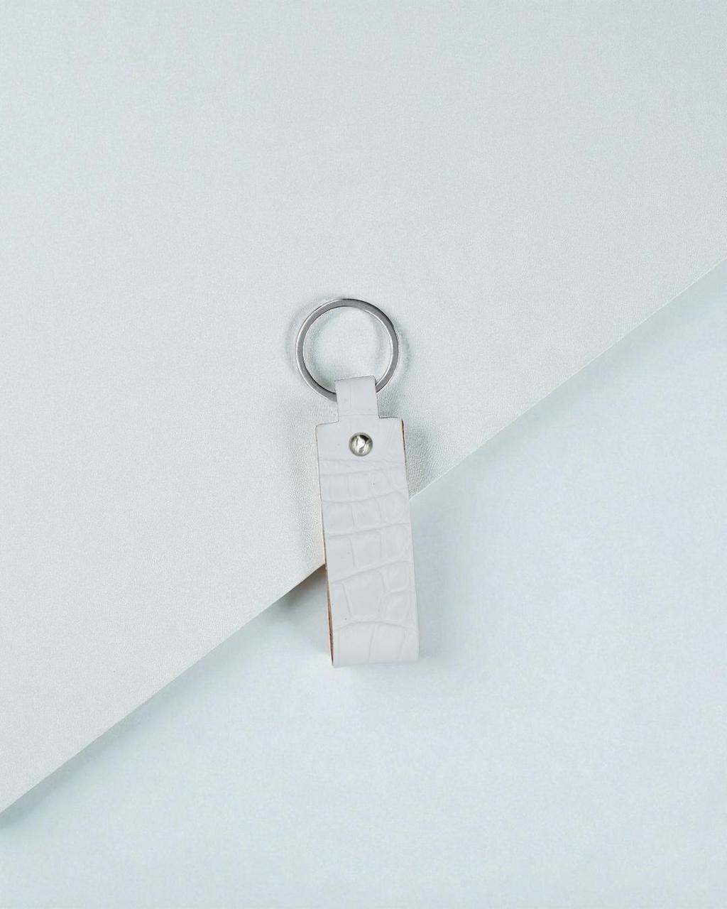A white faux-crocodile leather keychain with a silver metal key ring, resting on a clean white background.