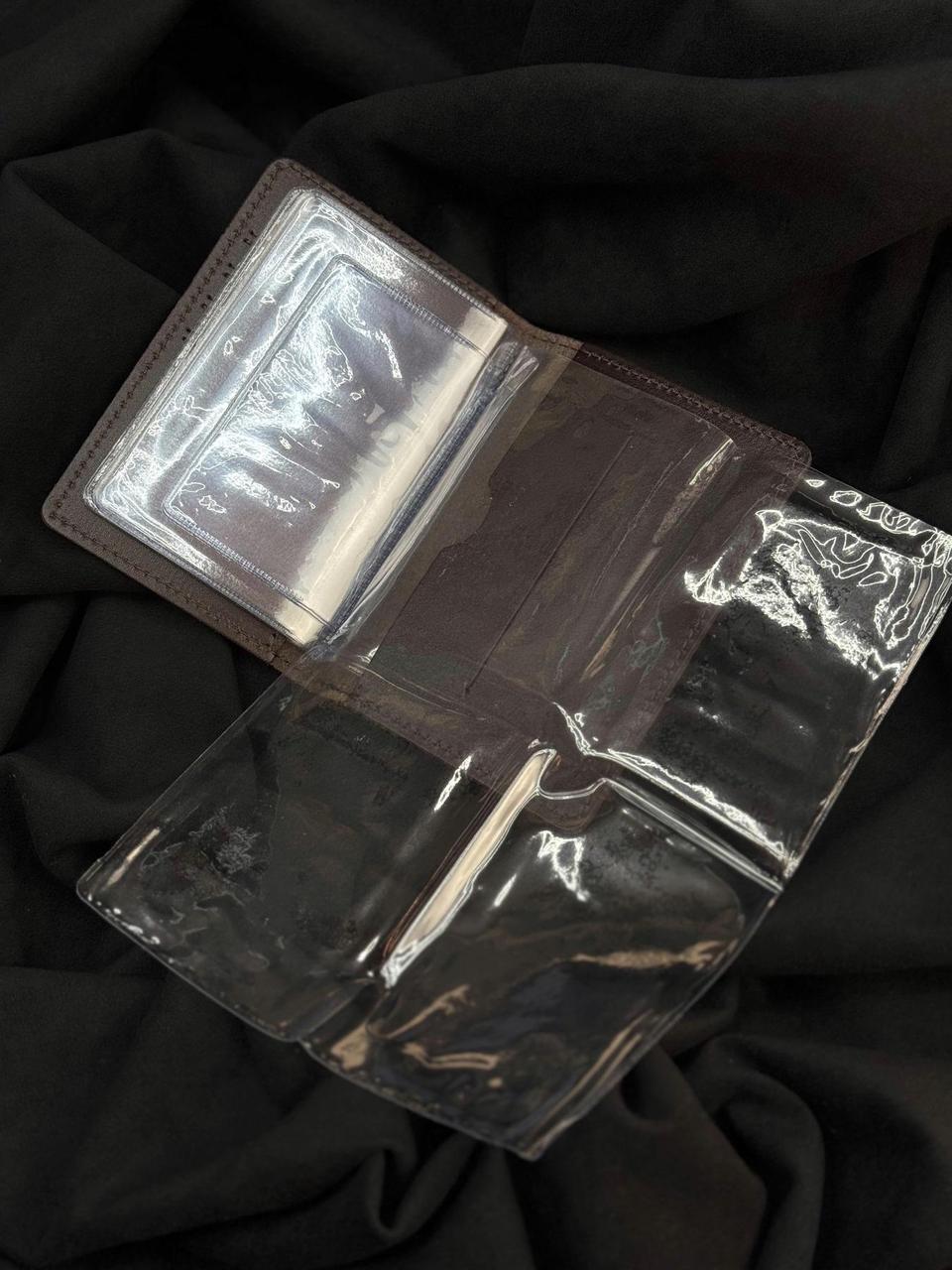 A clear plastic sleeve or cover with a brown border, shown open on a black fabric background. The transparent sections reveal card slots and compartments inside.