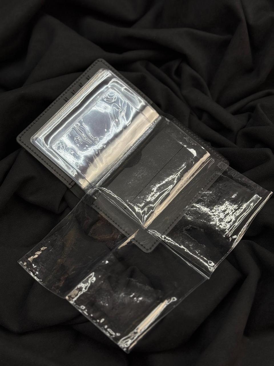 A clear plastic card holder or sleeve with black trim, shown open and laid on a black fabric background.