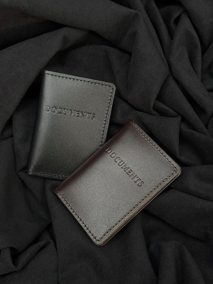 Two minimalist leather document wallets with the word 'DOCUMENTS' embossed on the front, displayed on a draped black fabric background.
