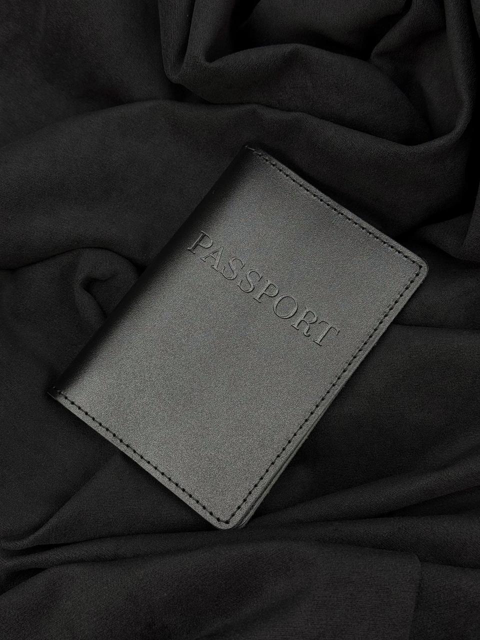 A dark gray faux-leather passport cover with 'PASSPORT' embossed on the front, resting on a draped black fabric background.