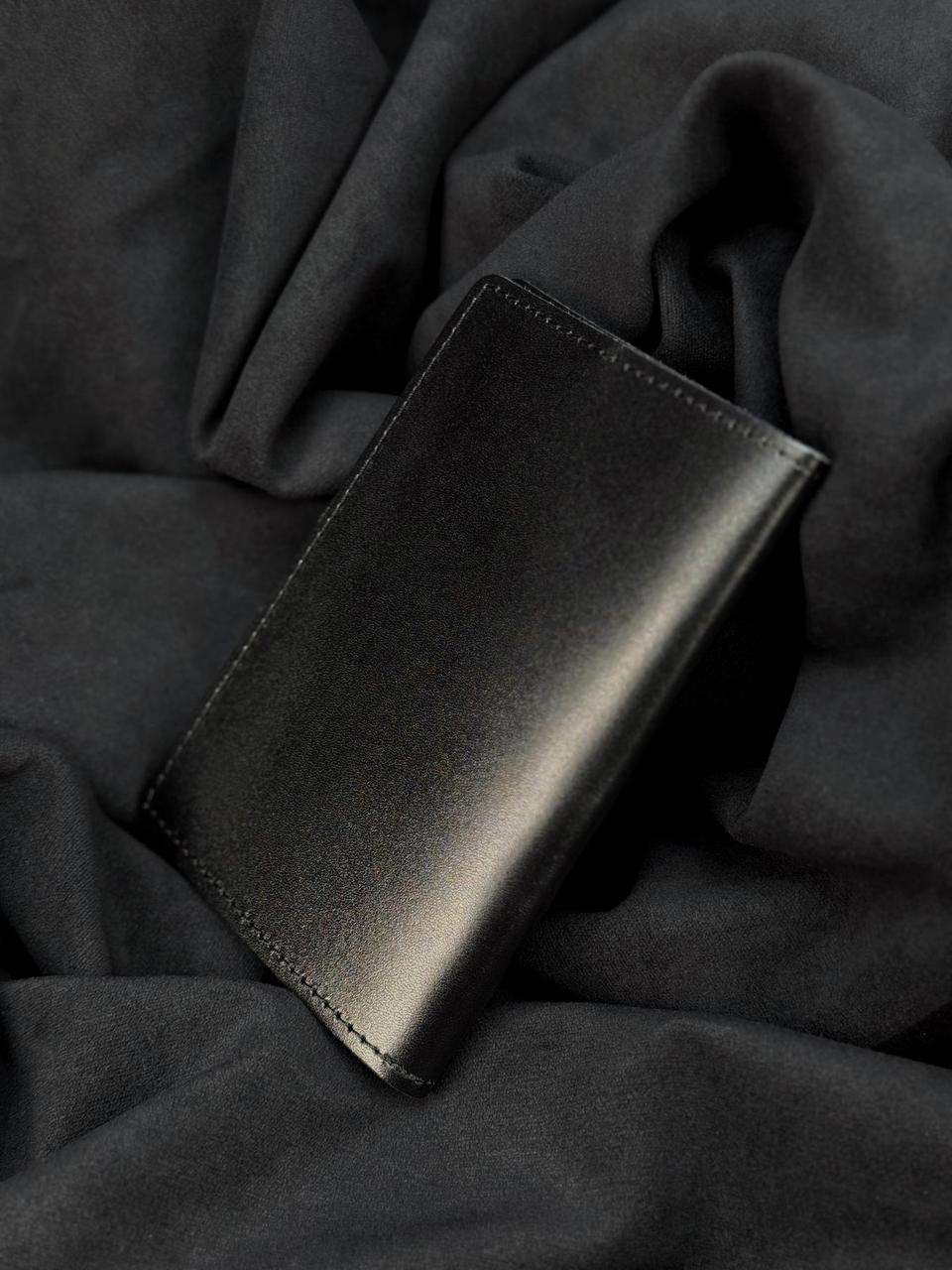 A minimalist black leather card holder wallet resting on a dark gray draped fabric background.