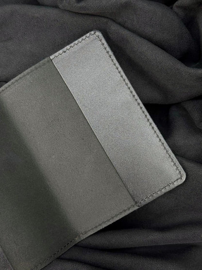 A close-up of a dark gray leather wallet or card holder with a stitched edge, placed on a matching dark gray fabric background.