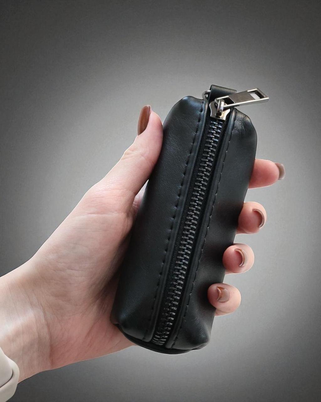 A hand holding a small black zippered pouch or case against a dark gray gradient background.