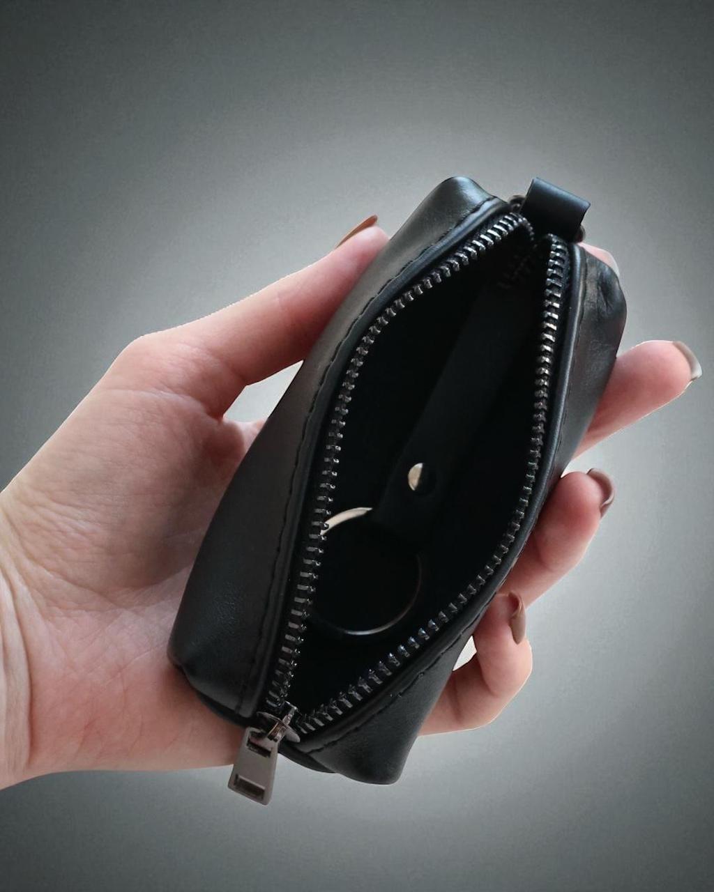 A hand holding an open black leather zippered pouch against a dark gray gradient background.