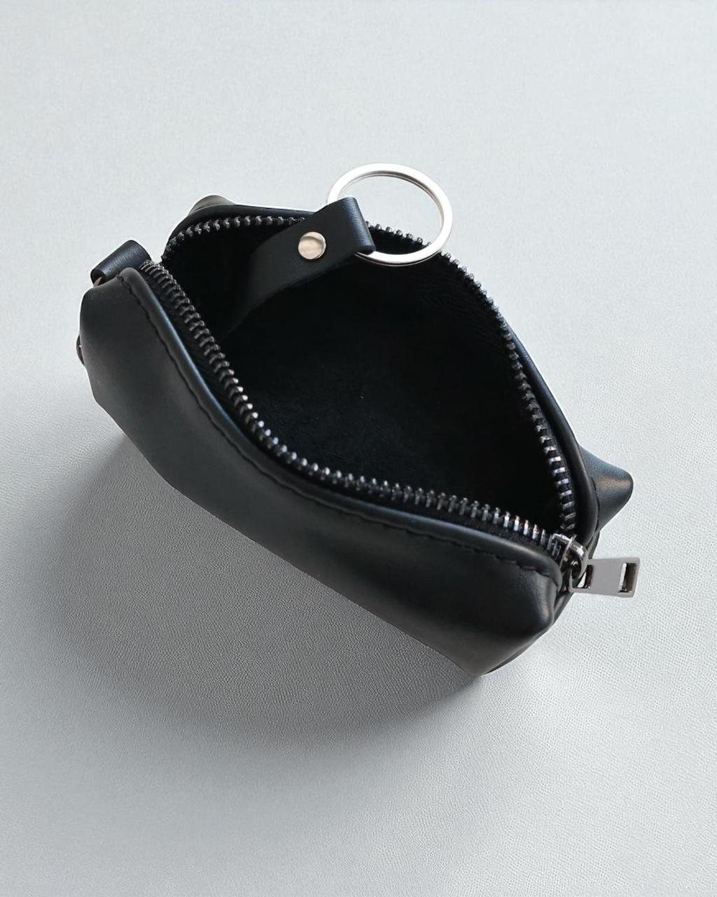 A small black leather zippered pouch with a silver metal key ring attachment, shown open on a light gray background.