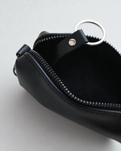 Close-up of a black leather zippered pouch with a silver metal key ring and a small silver rivet, shown open on a light gray background.