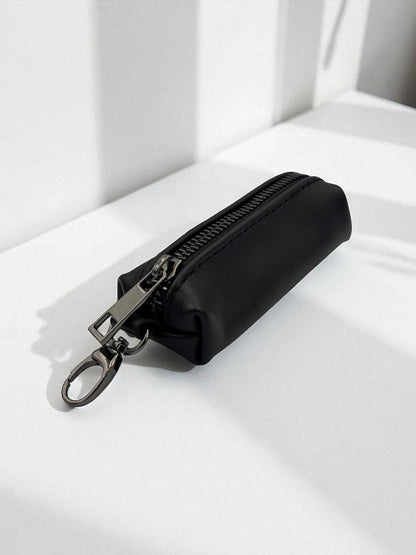 A small black zippered pouch with a silver metal key ring clasp, resting on a white surface with soft shadows.
