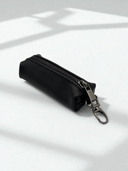 A small black zippered pouch with a silver metal clasp and key ring, photographed on a white surface with soft shadows.