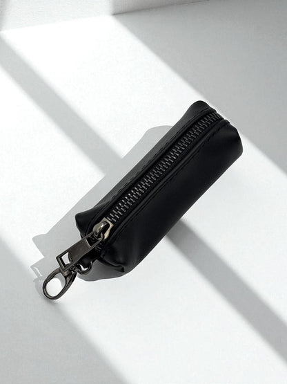 A small black zippered pouch with a silver-tone metal clasp and keychain ring, photographed on a white surface with sharp diagonal shadows.