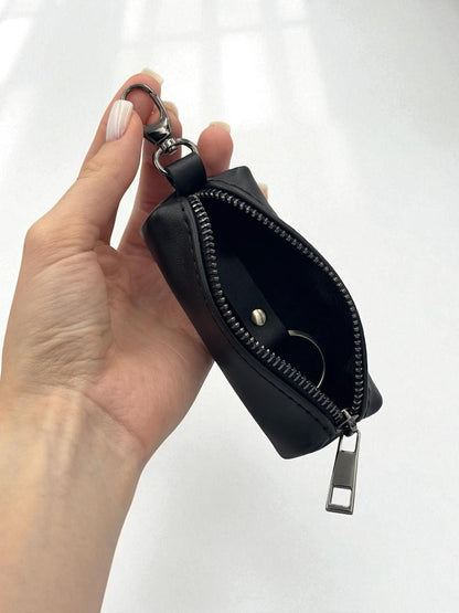 A hand holding a small black zippered pouch with a silver metal key ring and clasp, shown against a plain white background.