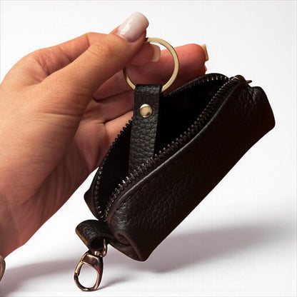 A hand holding a small black leather zip pouch with a gold-tone key ring and clasp, shown against a clean white background.