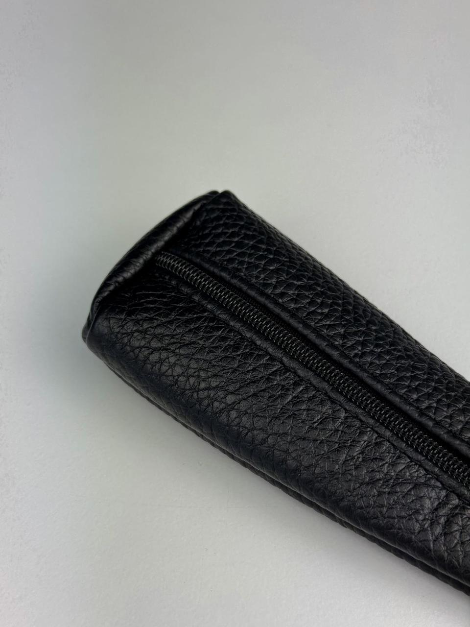 A close-up of a black pebbled leather zippered pouch or sleeve on a light gray background.