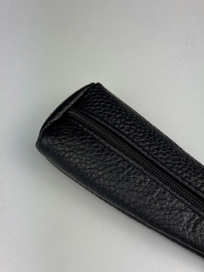 A close-up of a black pebbled leather zippered pouch or sleeve on a light gray background.