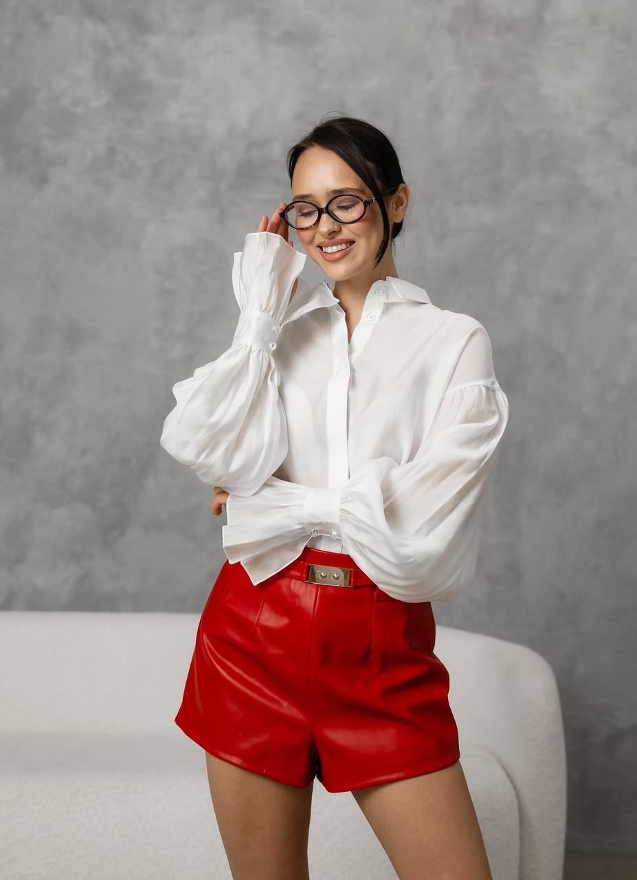 Woman wearing a white blouse and red shorts against a gray background