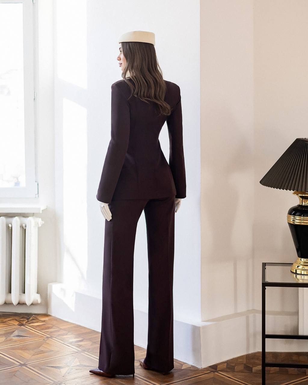 Woman in a dark suit standing in a room with a lamp and radiator.