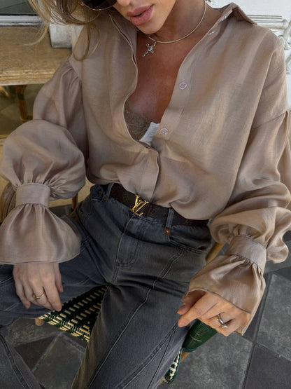 Person wearing a beige blouse with puffed sleeves and high-waisted jeans, sitting on a bench.