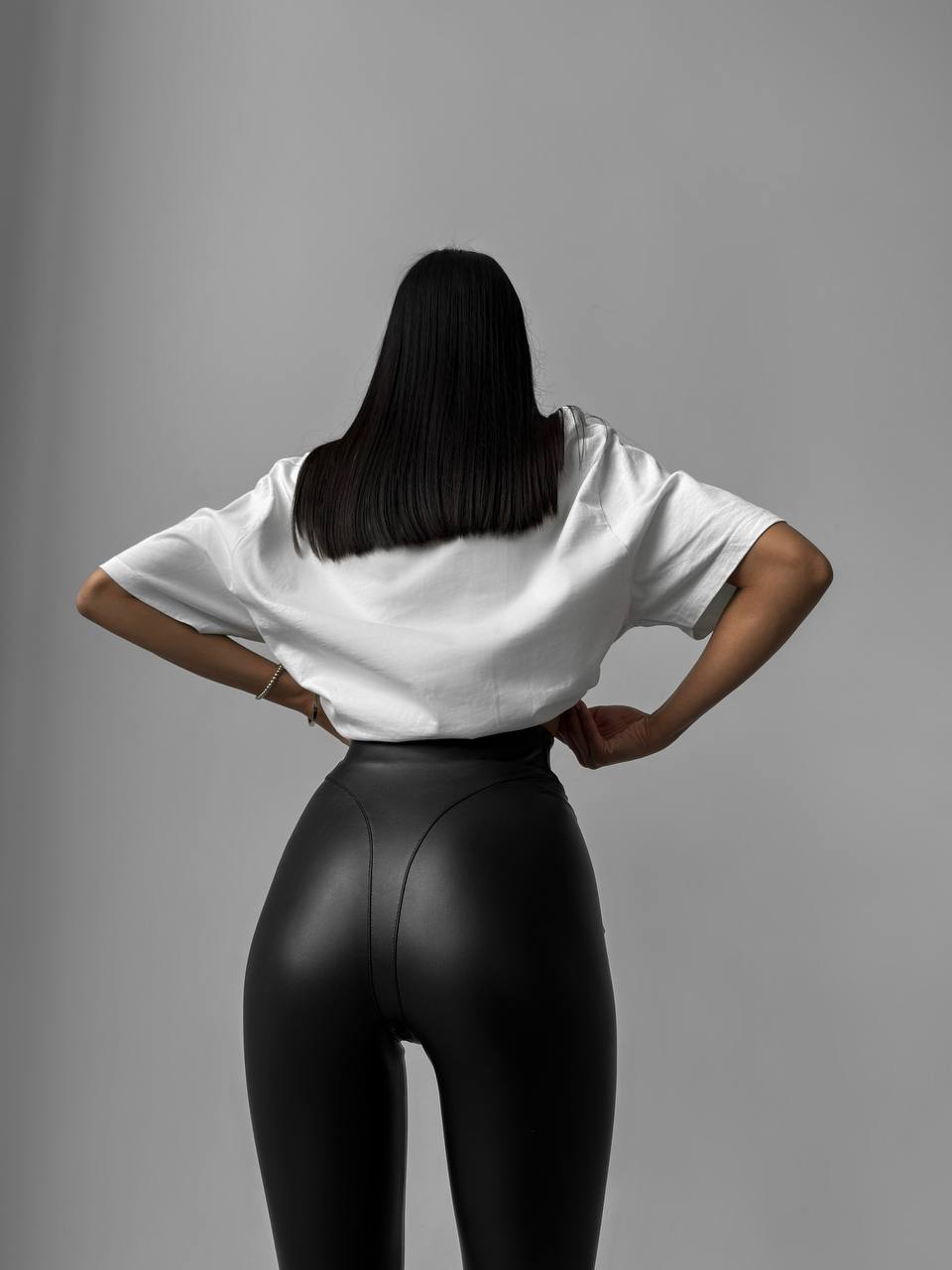 Person wearing a white shirt and black leggings against a gray background