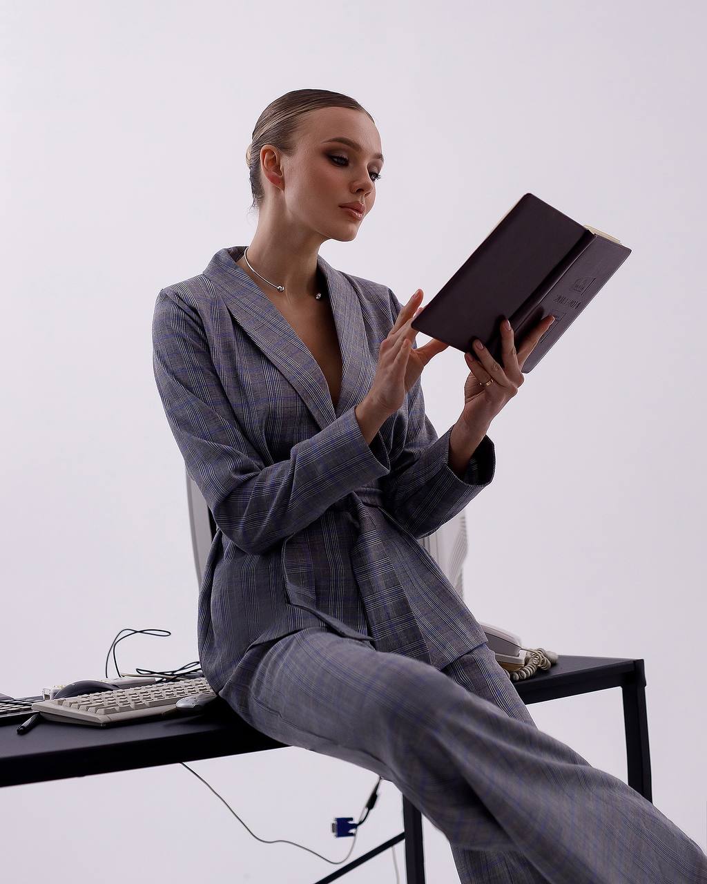 Woman in a gray suit sitting at a desk with a tablet on a white background