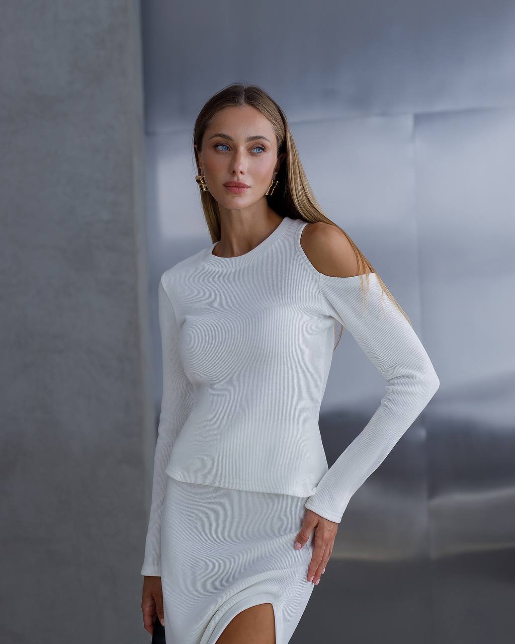 Woman wearing a white long-sleeve top and skirt against a gray background
