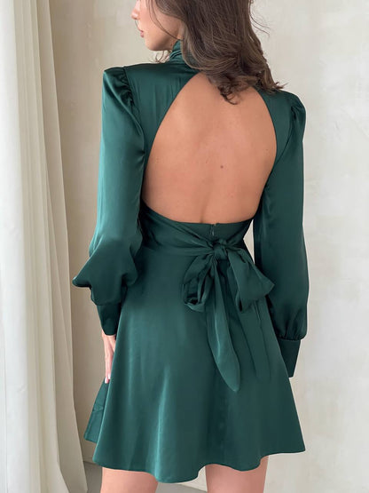 Green dress with open back and long sleeves on a neutral background