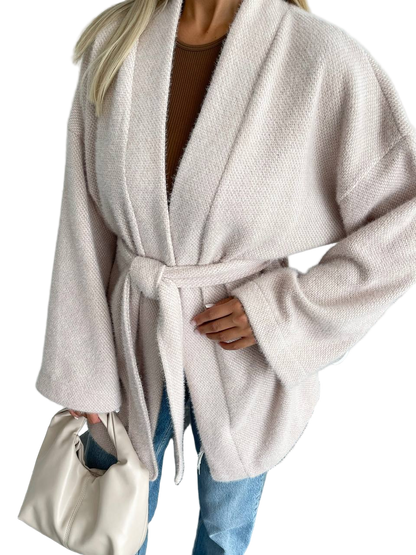 Person wearing a beige robe with a belt, holding a white handbag on a white background