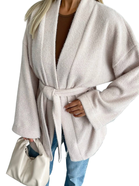 Person wearing a beige robe with a belt, holding a white handbag on a white background